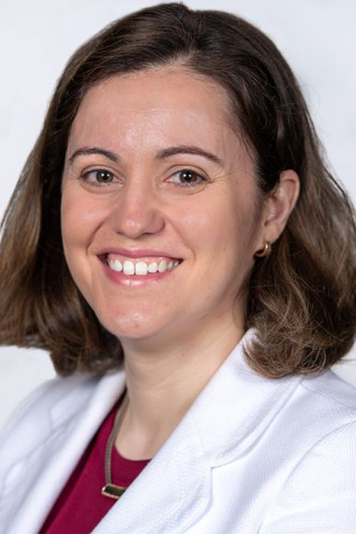 Woman smiling and looking at camera, wearing a white suit jacket.